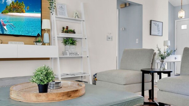 Ein Wohnzimmer mit Fernseher, einem Holztisch mit Pflanze, einem grauen Sofa und einem kleinen schwarzen Beistelltisch.