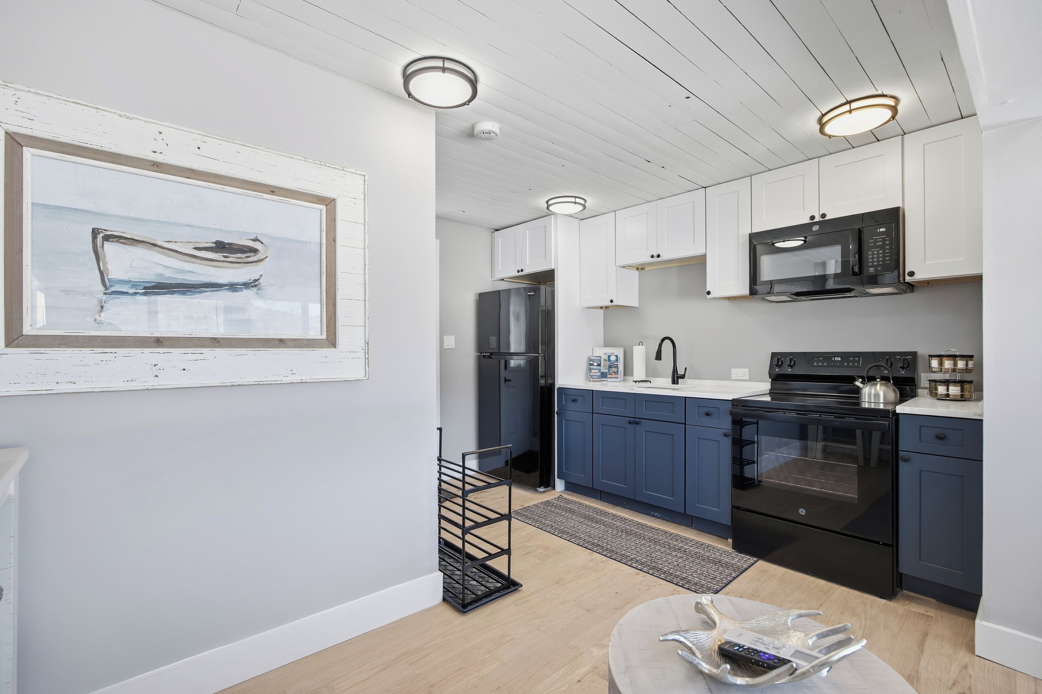 A modern kitchen with white and blue cabinets, a black refrigerator, a microwave, and a stove.