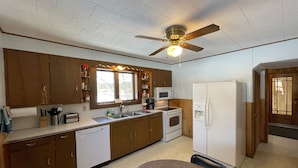 Una cocina compacta con armarios de madera, microondas integrado, refrigerador, lavavajillas y ventilador de techo.