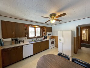 Une cuisine compacte avec des meubles en bois, un four à micro-ondes encastré, un réfrigérateur, un lave-vaisselle et un ventilateur de plafond.