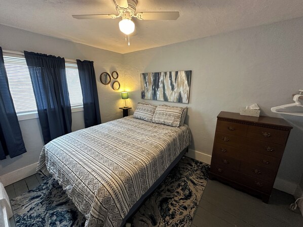 Une chambre à coucher comprenant un lit, une commode, une table de chevet avec une lampe et un ventilateur de plafond.