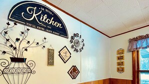 Una cocina con un letrero que dice 'Cocina abierta las 24 horas', un reloj y varios objetos decorativos en la pared.