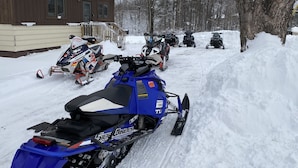Una moto de nieve estacionada en un sendero cubierto de nieve, con otras motos de nieve alineadas al fondo.