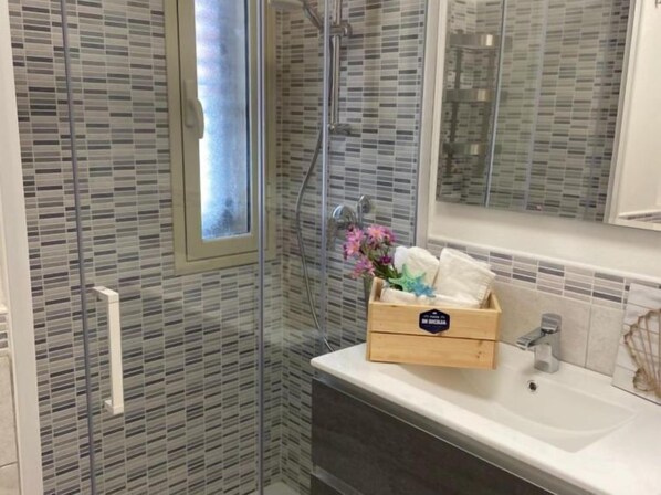 A modern bathroom with a glass shower enclosure, a wooden vanity with a sink, and a small window.
