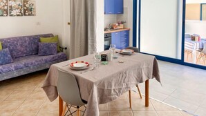 A dining area with a table set for two, a sofa, and a kitchen in the background. - Apartment Mare by Interhome (Santa Croce Camerina)