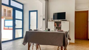 A dining area with a table set for two, a television on a cabinet, and a sliding glass door leading to an outdoor balcony. - Apartment Mare by Interhome (Santa Croce Camerina)