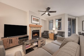 A living room with a flat-screen TV, fireplace, sofa, and a ceiling fan.