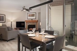 A dining area with a wooden table set for four, a fireplace, a ceiling fan, and a television.