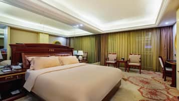 A hotel room with a large bed, a desk with a telephone, two chairs, and a desk lamp.