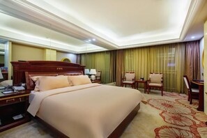 Ein Hotelzimmer mit einem großen Bett, einem Schreibtisch mit Telefon, zwei Stühlen und einer Schreibtischlampe.