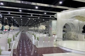 Un espacio con filas de sillas blancas, un pasillo central y un escenario con un telón de fondo blanco.