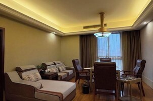 A hotel room with a sofa, chairs, a dining table, and a chandelier.