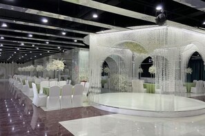 A banquet hall with a central stage, white chairs, and floral centerpieces. - Aoti Hotel (Wuhu)