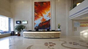 Uma área de recepção com uma grande pintura abstrata, um balcão de atendimento, plantas em vasos e um chão polido com padrão floral.