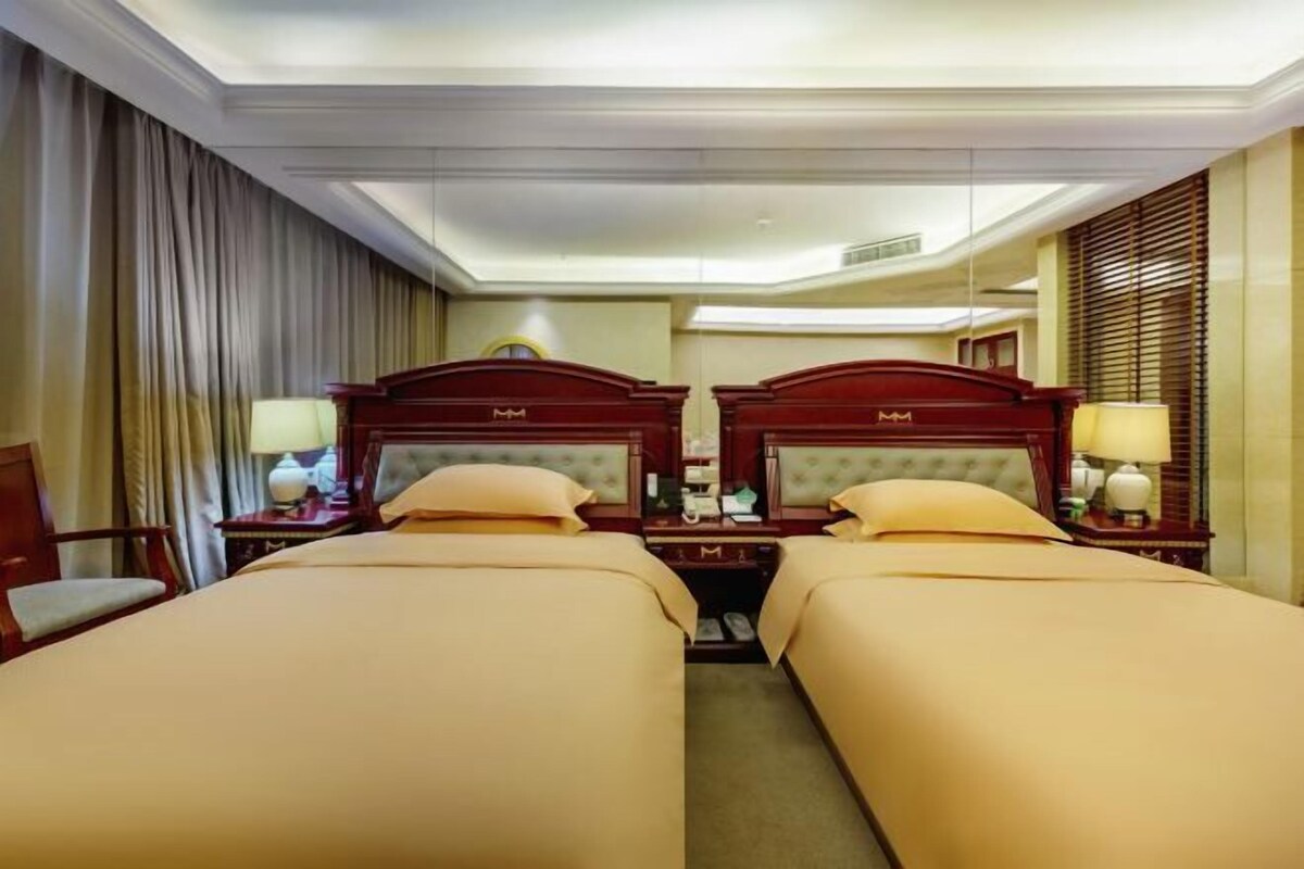 Ein Hotelzimmer mit zwei Betten, jeweils mit einem Holz-Kopfstück, einem Nachttisch mit Lampe und einem Spiegel.