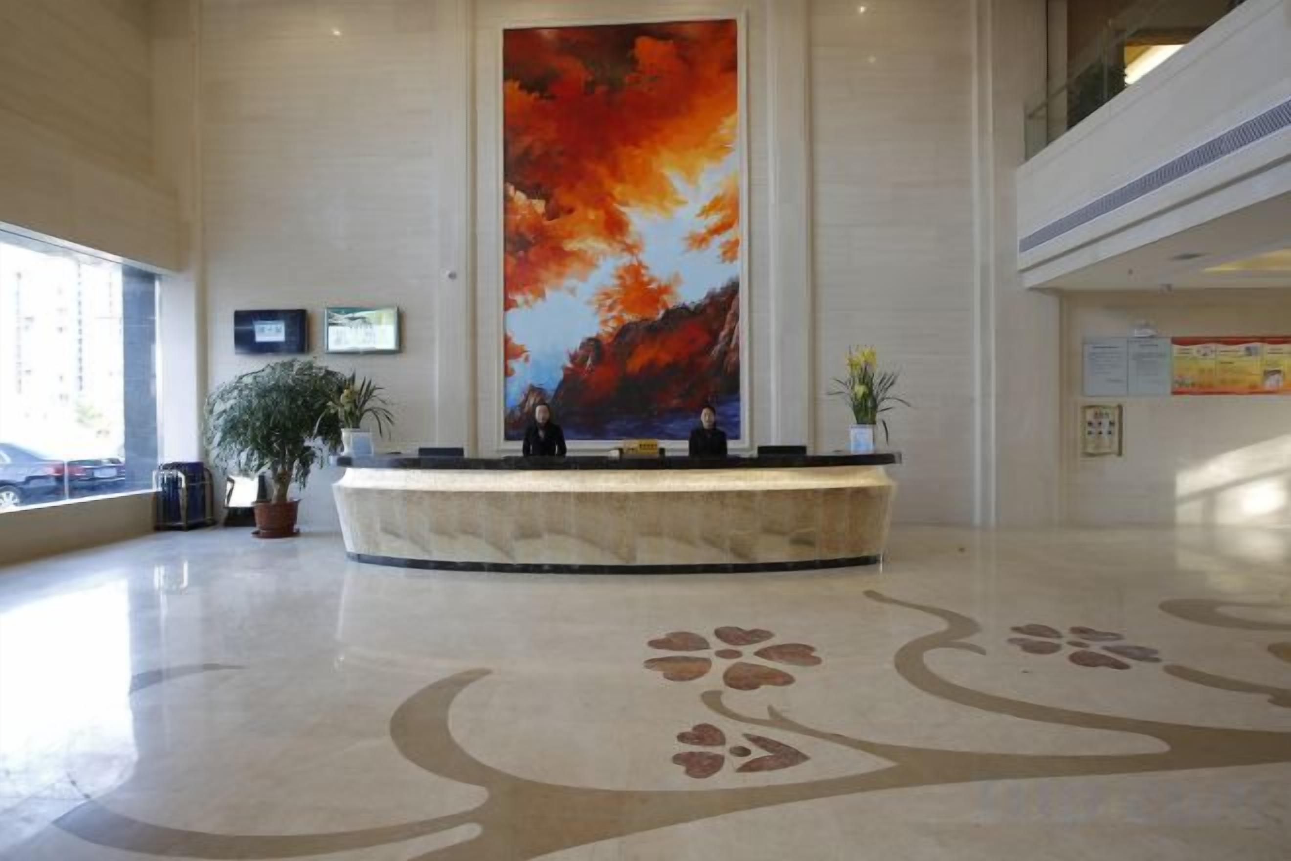 A reception area with a large painting, a reception desk, potted plants, and a patterned floor.