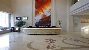 A reception area with a large painting, a reception desk, potted plants, and a patterned floor.