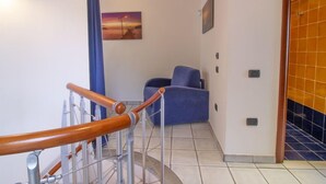 Eine Treppe mit hölzernen Geländern, ein blauer Stuhl und ein Sonnenuntergangsbild an der Wand.