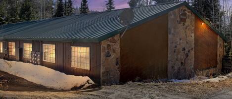 A rustic cabin with a metal roof, large windows, and a stone exterior.