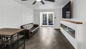 A modern living room with a dark wood floor, a leather sofa, a dining table with metal shelves, a ceiling fan, and a fireplace with a glass enclosure. - Beautiful Ski-in/ski-out Condo Located On The Eagle Point Resort! 1 Bedroom Condo by RedAwning (Beaver)