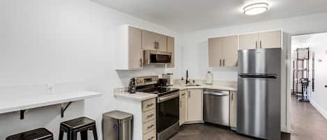 Una cocina moderna con paredes blancas, armarios de madera, electrodomésticos de acero inoxidable y un suelo de madera en espiga.