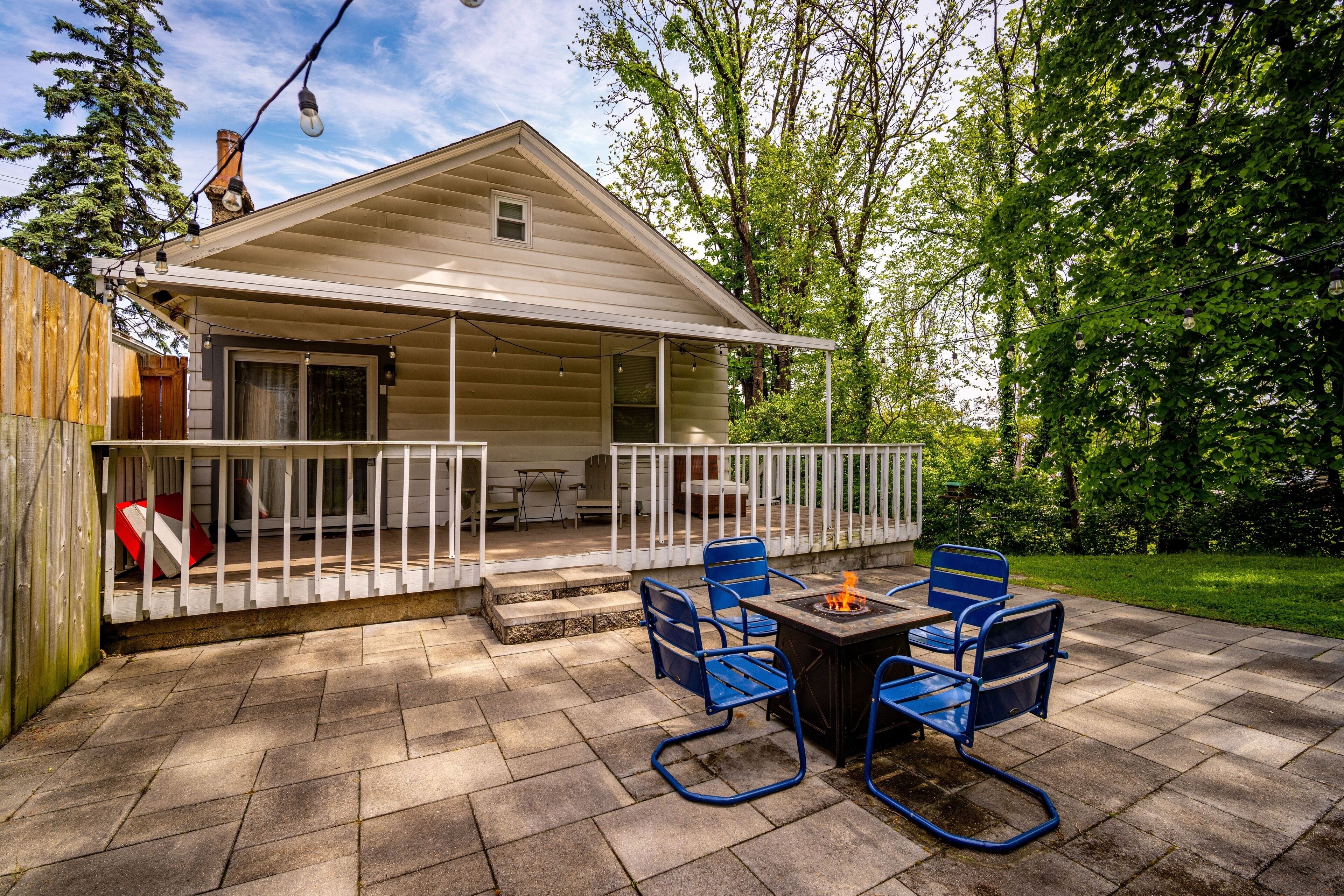 A covered patio with stone flooring, a fire pit, and blue metal chairs.