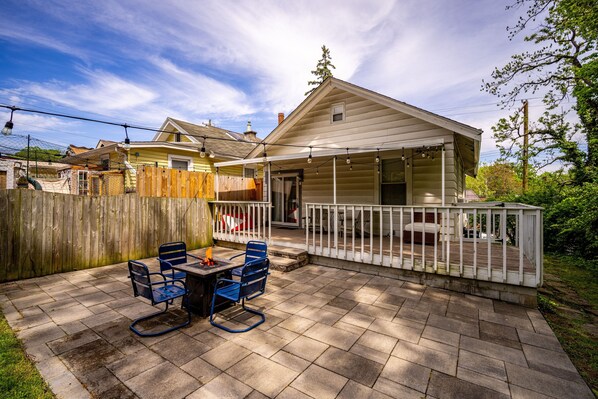 A patio with a table and chairs, a covered deck, and a house in the background.