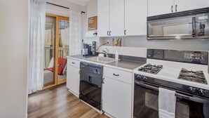 Una cocina compacta con armarios blancos, microondas integrado, cocina a gas y lavavajillas.