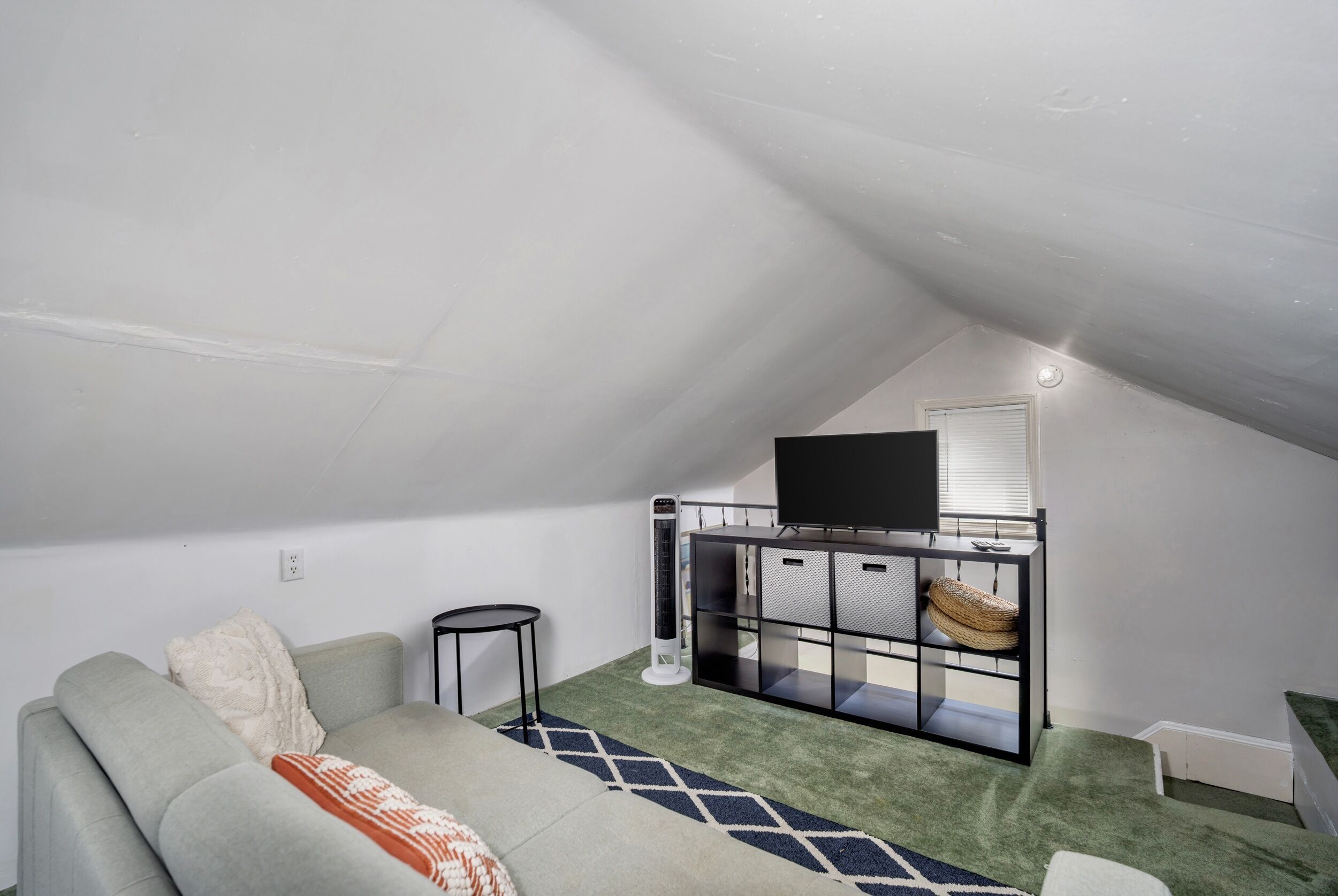 A small, cozy attic room with a sofa, a TV on a stand, and a small table.