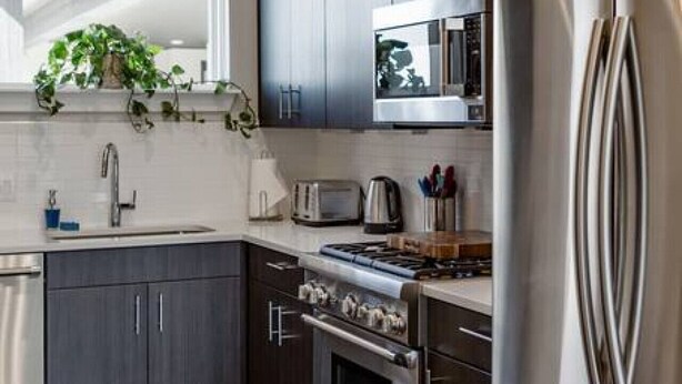 A modern kitchen with dark wood cabinets, stainless steel appliances, a microwave, a stove, and a refrigerator. - Capitol View Condos by One Fine Bnb - Paramount (Austin)