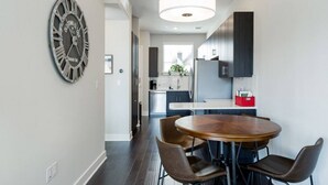 A modern kitchen with dark cabinets, a wooden dining table, and a large wall clock. - Capitol View Condos by One Fine Bnb - Paramount (Austin)