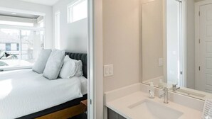 A modern hotel room with a bed, a large window, a bathroom with a sink and mirror, and a view of the street. - Capitol View Condos by One Fine Bnb - Paramount (Austin)