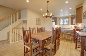 Un vaste espace dédié à la salle à manger, avec une table et des chaises en bois, un lustre, et une vue sur la cuisine et l’extérieur.
