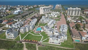 Vista aérea de un resort con varias edificaciones, una piscina central y abundante vegetación.