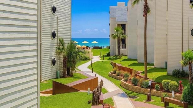 Un resort con un camino que lleva a una zona de piscina, rodeado de palmeras y vistas al océano.