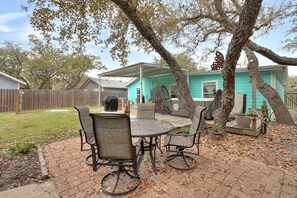 Une terrasse extérieure avec une table ronde et des chaises, entourée d’arbres et avec une maison en arrière-plan.