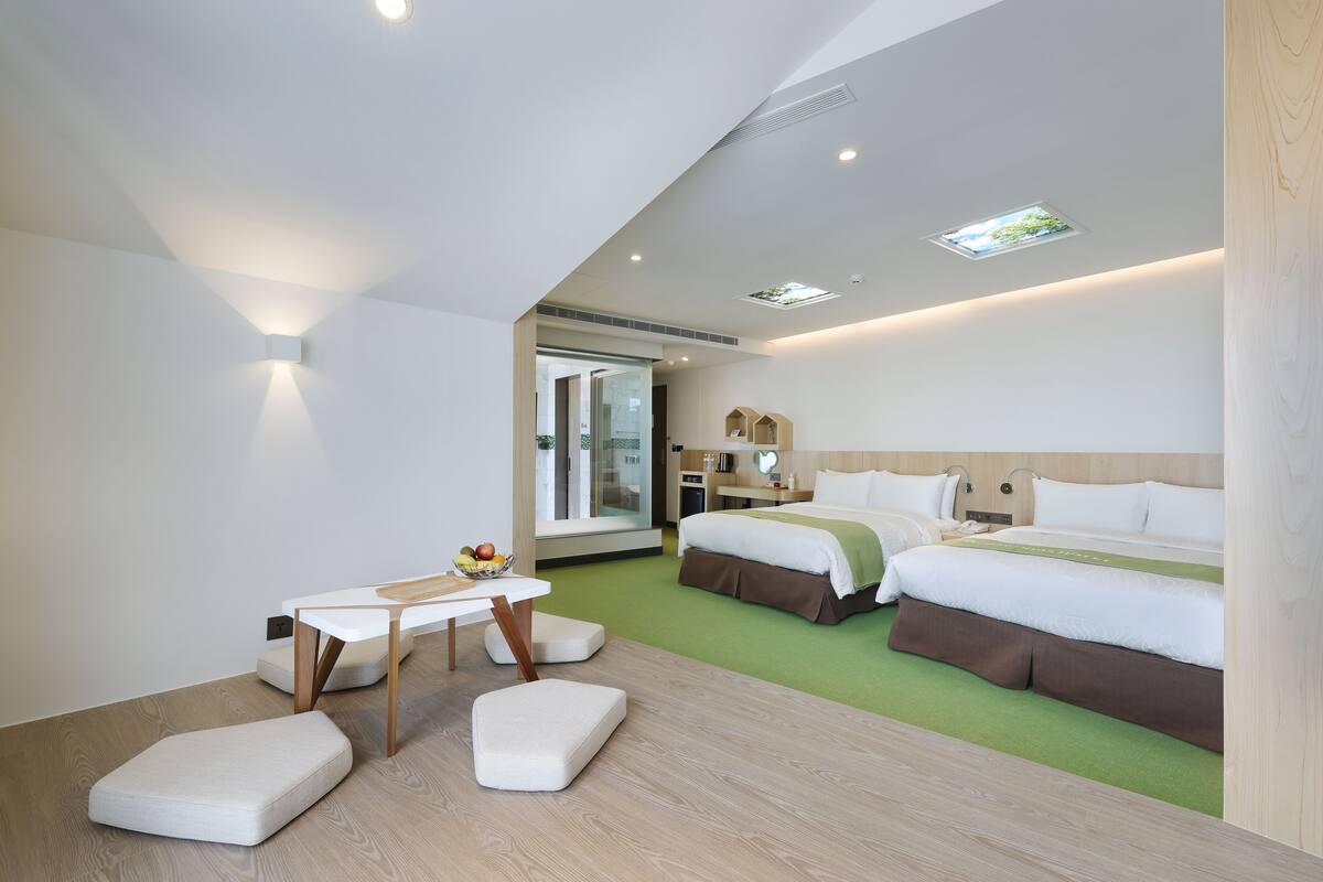 Ett modernt hotellrum med en stor säng, ett litet bord med en fruktskål och en grön matta.