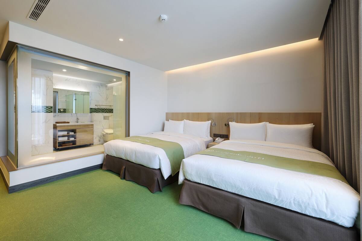 Ett hotellrum med två sängar, en stor spegel, en sminkbord och en grön matta.
