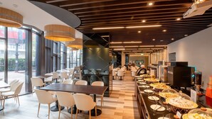 A modern cafeteria with long communal tables and individual seating, a buffet area with various food options, and a view through large windows. - CHECK inn MAGI Kids (Luodong)