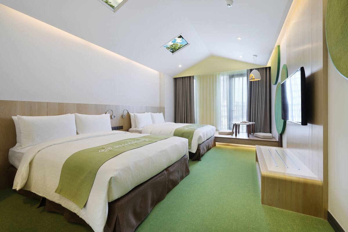 Ett hotellrum med två sängar, ett litet bord, en TV och en taklampa.