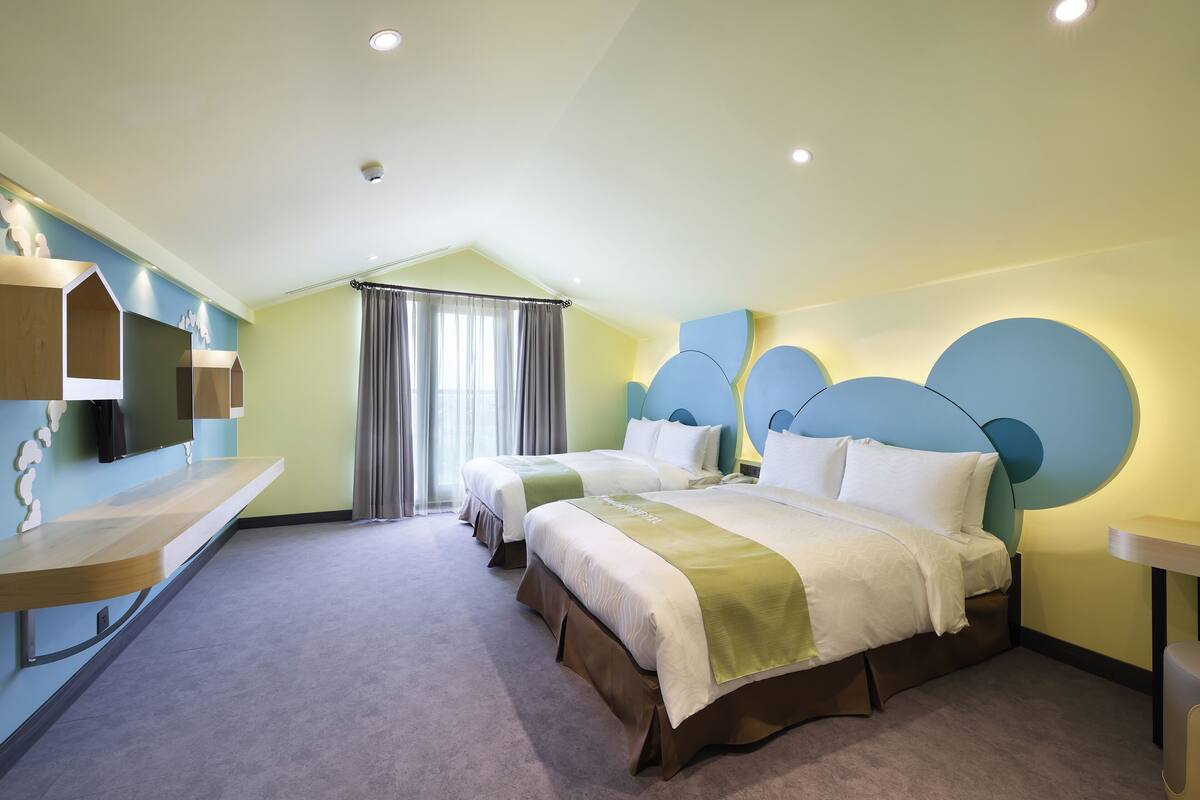 Ett hotellrum med två sängar, ett skrivbord och ett stort fönster med gardiner.