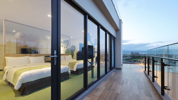 A modern hotel room with a large bed, a desk, and a view of the city through floor-to-ceiling windows. - CHECK inn MAGI Kids (Luodong)