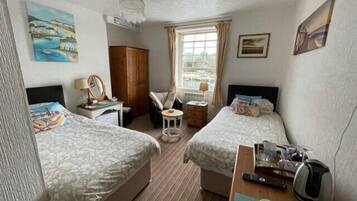 A hotel room with two beds, a desk, a chair, a small table, a window with curtains, and artwork on the walls.