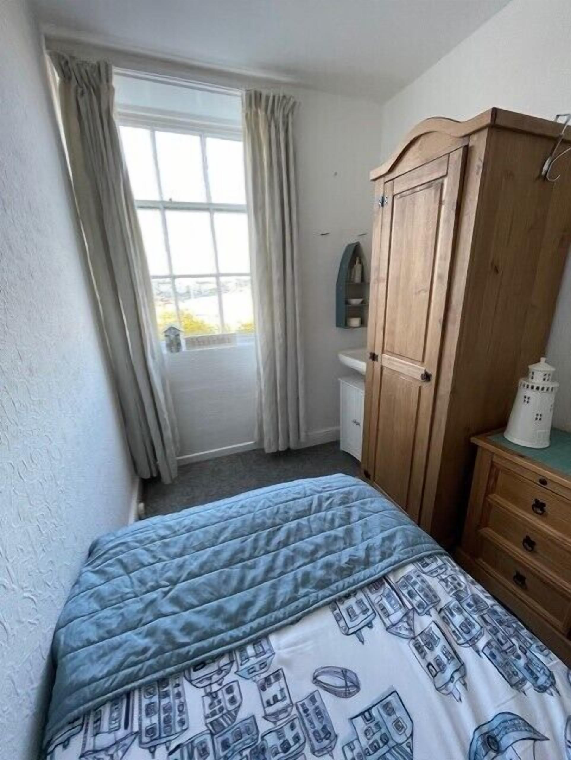 A bedroom with a bed, a wooden wardrobe, a window with curtains, and a view of the outside.