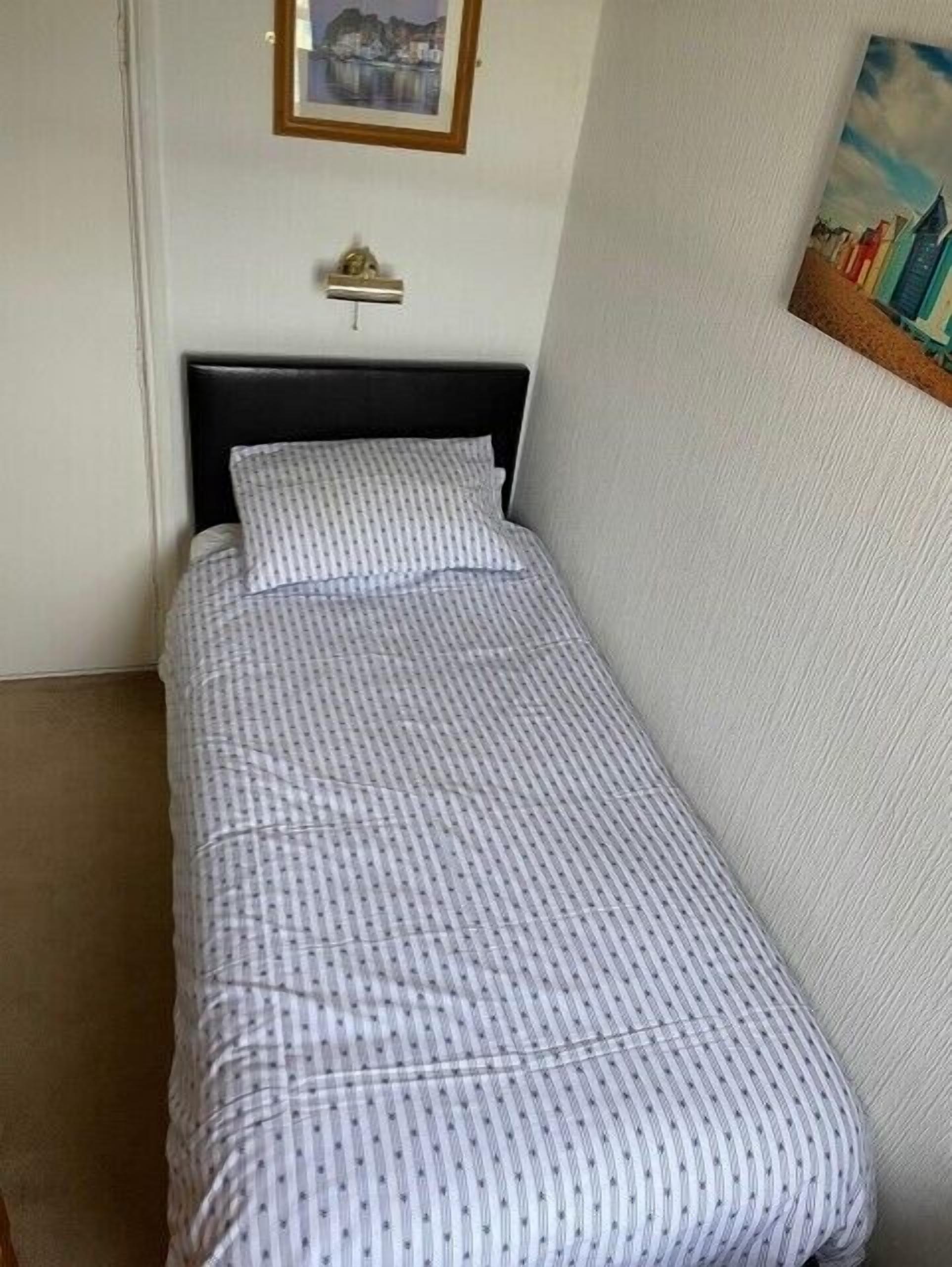 A single bed with a patterned bedspread in a room with plain walls.