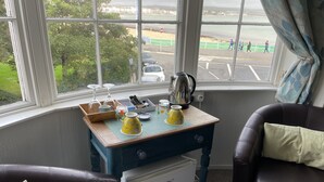 Habitació acollidora amb vista a la platja, una taula petita amb joc de te i un frigorífic.