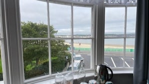 Una taula amb servei de te i gots a prop d'una finestra amb vista a una platja i un aparcament.