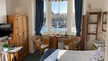 A room with a bed, two chairs, a desk, a television, and a view of a body of water through a window.