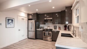 A modern kitchen with stainless steel appliances, a marble countertop, and dark cabinetry. - Scenic Waterfront Getaway Townhouse with Kayak! (Oxnard)