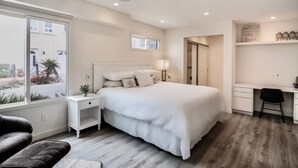 A modern bedroom with a large bed, bedside tables, a desk, and a chair. - Scenic Waterfront Getaway Townhouse with Kayak! (Oxnard)